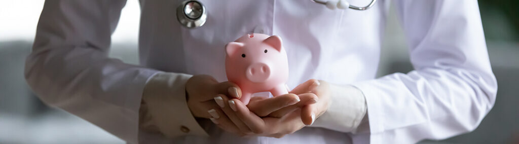 A pink piggy bank that is being held with two hands by a person in a white coat and a stethoscope
