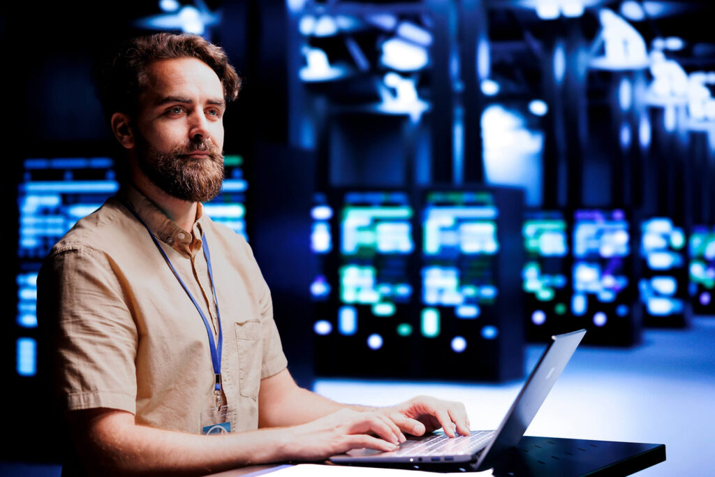 Person on laptop typing in server room answering inquiries in real-time.