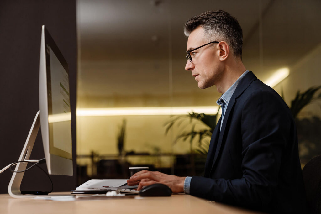 mature man working on the computer at a desk in an office reviewing edi services automation results