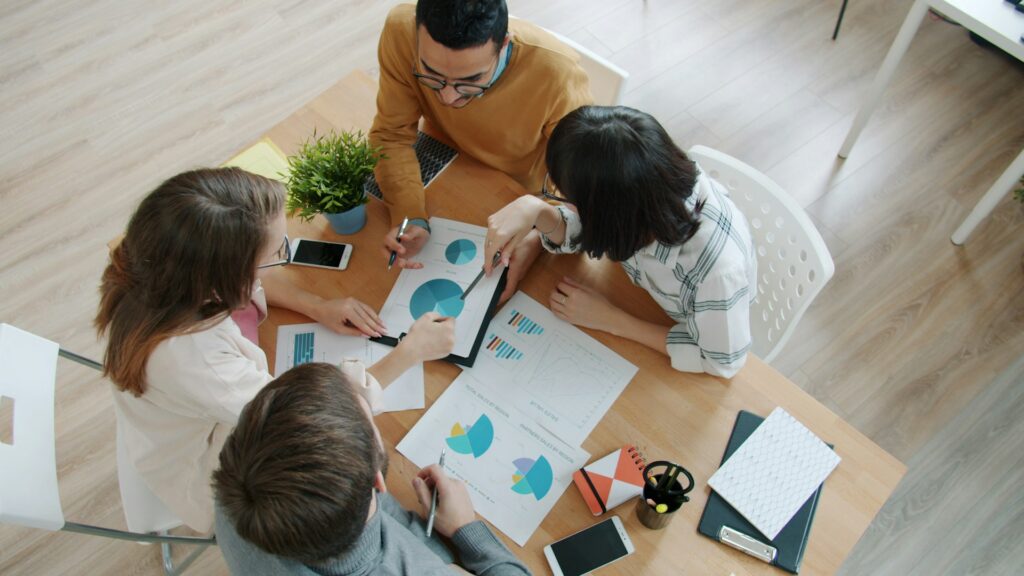 A group of four people sitting at a table analyzing graphs.