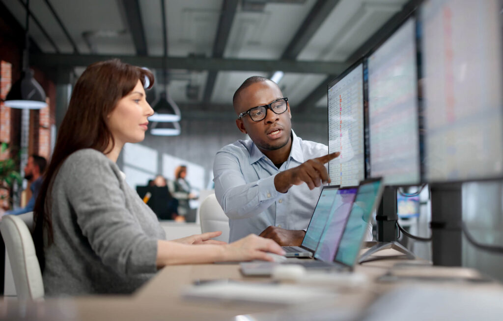 man pointing at computer monitors and a woman using a laptop